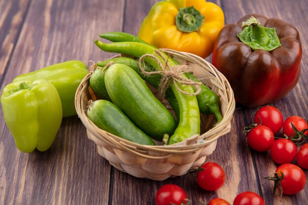 Seitenansicht des Gemüses im Korb als Pfeffer und Gurke mit Tomaten herum auf Holz