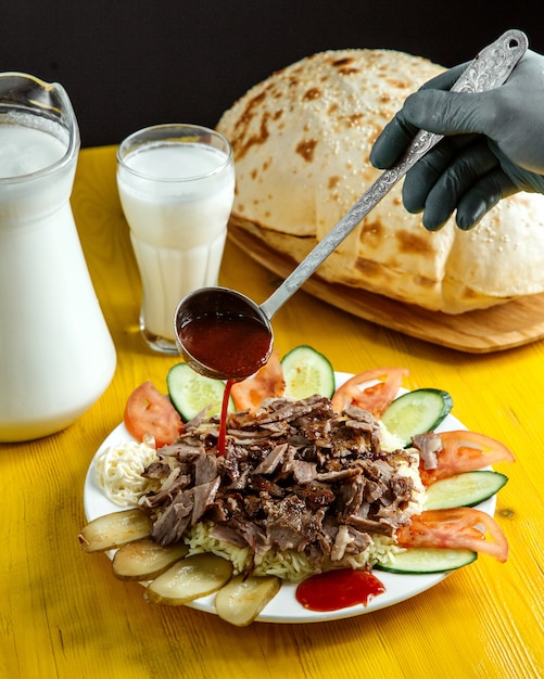 Seitenansicht des Gießens der Soße auf Döner auf Teller serviert mit Gurken frischen Gurken und Tomaten