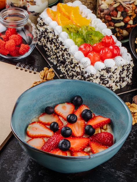 Kostenloses Foto seitenansicht des haferbrei mit geschnittenen erdbeeren und blaubeeren in einer keramikschale auf dem tisch