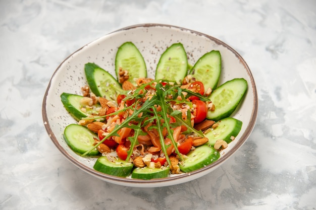 Seitenansicht des hausgemachten gesunden köstlichen veganen Salats, der mit gehackten Gurken in einer Schüssel auf befleckter weißer Oberfläche verziert wird