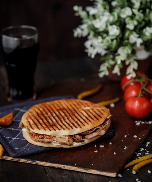 Seitenansicht des Hühnchen-Döner-Kebabs im Fladenbrot und auf einem Holzbrett und Tomaten auf dem Tisch