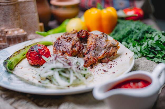 Seitenansicht des Hühnerkebabs mit Zwiebelkräutern und gegrilltem Gemüse auf einem weißen Teller