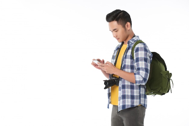 Seitenansicht des jungen asiatischen Touristen mit Rucksack unter Verwendung des Smartphone