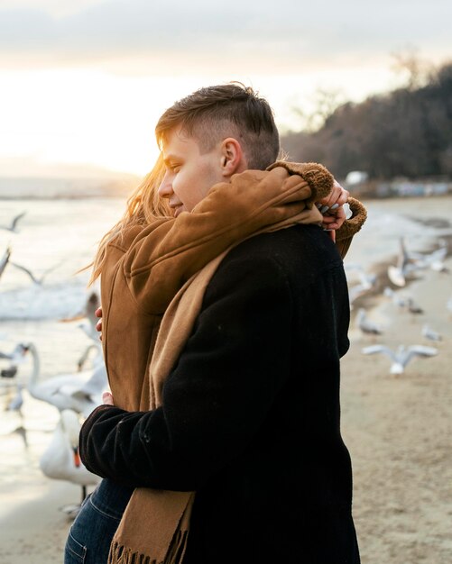 Seitenansicht des jungen Paares, das im Winter am Strand umarmt