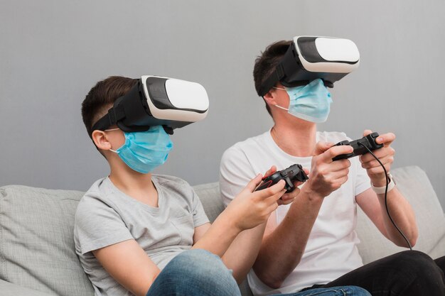 Seitenansicht des Jungen und des Mannes, die mit dem Virtual-Reality-Headset beim Tragen von medizinischen Masken spielen