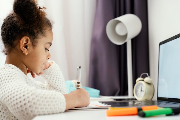 Seitenansicht des kleinen Mädchens, das Online-Schule zu Hause unter Verwendung des Laptops besucht