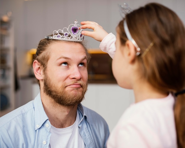 Seitenansicht des kleinen Mädchens, das Tiara auf Vaters Kopf setzt