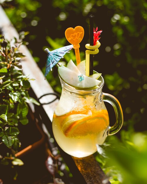 Seitenansicht des Kruges der Limonade mit Zitronen und Strohhalmen am grünen Hintergrund