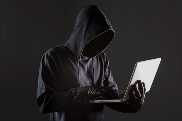 Seitenansicht des männlichen Hackers mit Handschuhen und Laptop