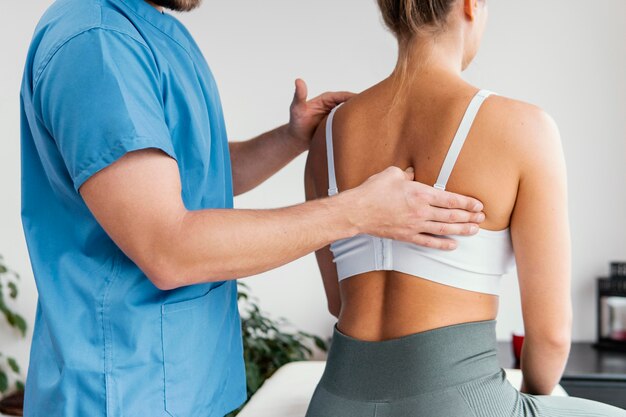 Seitenansicht des männlichen osteopathischen Therapeuten, der das Schulterblatt des weiblichen Patienten prüft