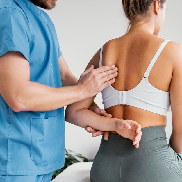 Seitenansicht des männlichen osteopathischen Therapeuten, der das Schulterblatt des weiblichen Patienten prüft