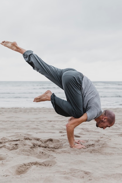 Seitenansicht des Mannes am Strand, der Yoga-Positionen praktiziert