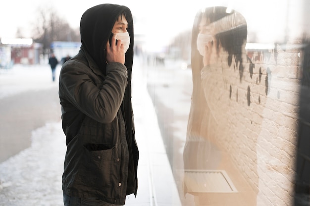 Kostenloses Foto seitenansicht des mannes, der am telefon spricht, während er draußen eine medizinische maske trägt