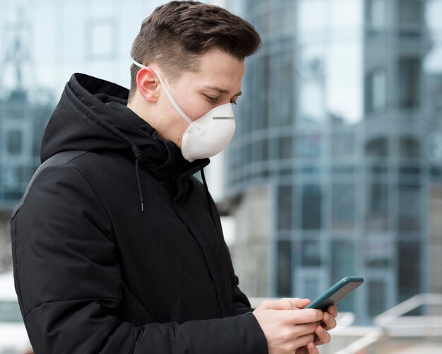 Seitenansicht des Mannes, der sein Telefon beim Tragen einer medizinischen Maske betrachtet