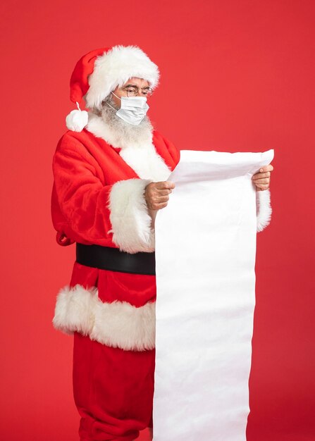 Seitenansicht des Mannes im Weihnachtsmannkostüm mit der medizinischen Maske, die Geschenkliste hält