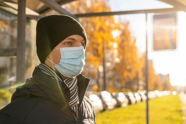 Kostenloses Foto seitenansicht des mannes mit der medizinischen maske, die auf den bus wartet