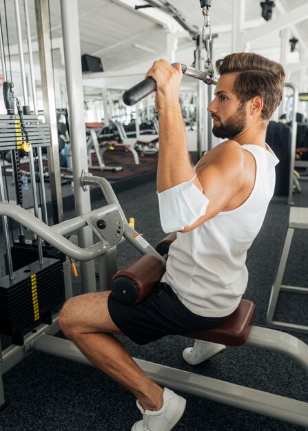 Seitenansicht des Mannes mit medizinischer Maske auf seinem Unterarm, der im Fitnessstudio trainiert