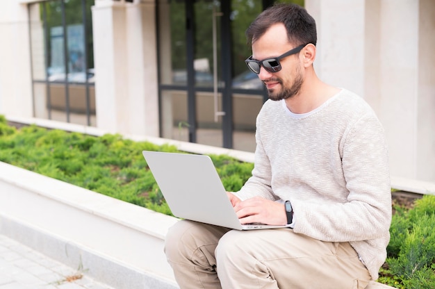 Seitenansicht des Mannes mit Sonnenbrille, die auf Laptop im Freien arbeitet