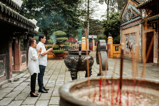 Seitenansicht des Mannes und der Frau, die am Tempel mit brennendem Weihrauch beten