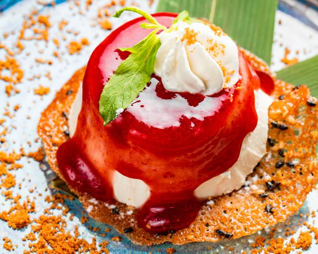Seitenansicht des Minikuchens bedeckt mit Schlagsahne und Erdbeersirup und Minzblatt auf einem Teller