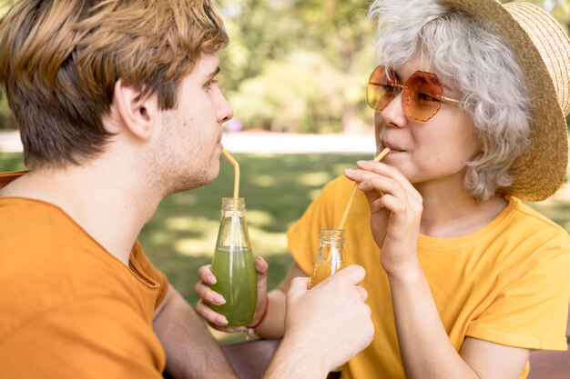 Seitenansicht des niedlichen Paares, das Saft im Park mit Strohhalmen trinkt