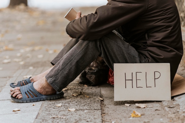 Seitenansicht des Obdachlosen auf der Straße mit Tasse und Hilfeschild