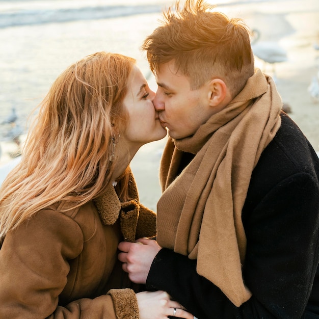 Kostenloses Foto seitenansicht des paares, das im winter zusammen am strand küsst und spaß hat