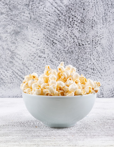 Seitenansicht des Popcorns in der Schüssel auf weißem Holztisch vertikal