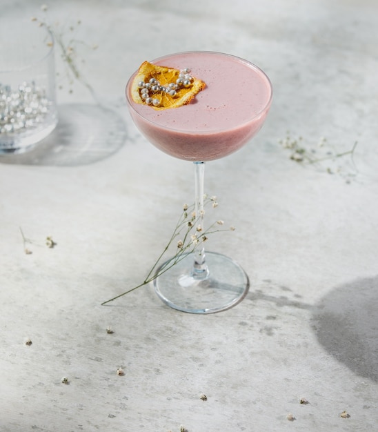 Kostenloses Foto seitenansicht des rosa fruchtcocktails verziert mit getrockneter orangenscheibe in einem glas auf weißer wand