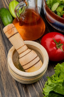 Seitenansicht des schwarzen pfeffers im knoblauchbrecher mit geschmolzenem ölsalat-tomaten-gurkensalz und gemüsesalat auf holzoberfläche