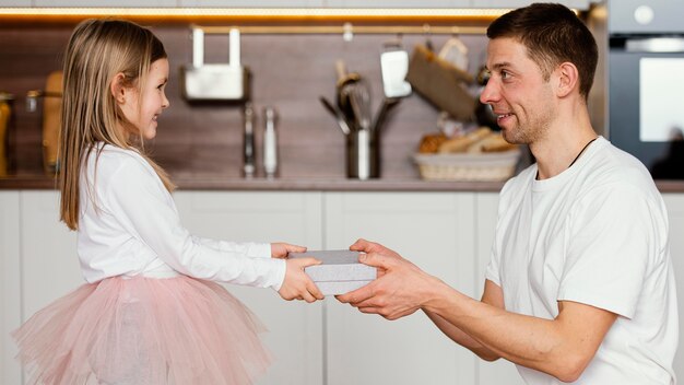 Seitenansicht des Smiley-Mädchens im Tutu-Rock, das ihrem Vater ein Geschenk für den Vatertag gibt