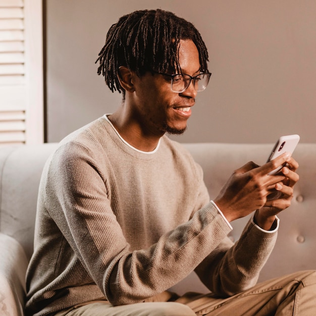 Kostenloses Foto seitenansicht des smiley-mannes zu hause unter verwendung des smartphones