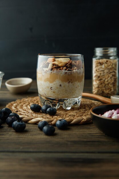 Seitenansicht des Smoothie mit Bananen-Mandel-Walnuss-Milch-Erdnussbutter mit Schwarzdorn auf Untersetzer auf Holzoberfläche und schwarzem Hintergrund