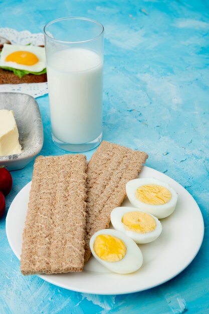 Seitenansicht des Tellers der Knäckebrote und der Eier mit Glas Milch auf blauem Hintergrund mit Kopienraum