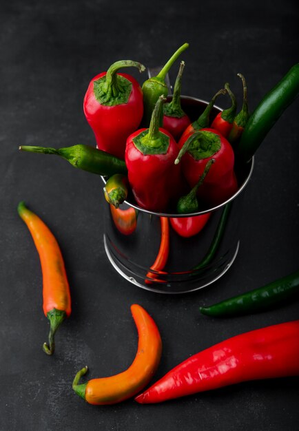 Seitenansicht des Topfes voll Paprika mit anderen Paprikaschoten herum auf schwarzem Hintergrund