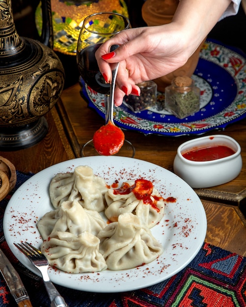 Seitenansicht des traditionellen georgischen Khinkali und einer Frauenhand, die einen Löffel mit würziger Tomatensauce hält