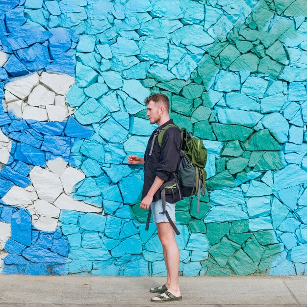 Seitenansicht des tragenden Rucksacks des jungen Reisendmannes gegen Steinwand