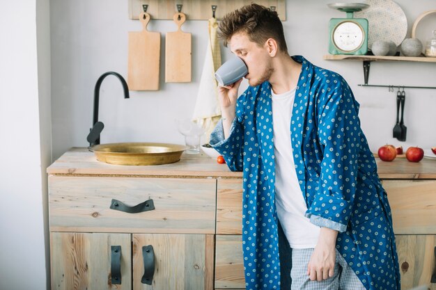 Seitenansicht des trinkenden Kaffees des Mannes, der zu Hause nahe Wanne steht