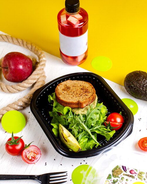 Seitenansicht des veganen Sandwichs mit Avocado und Tomaten in der Lieferbox