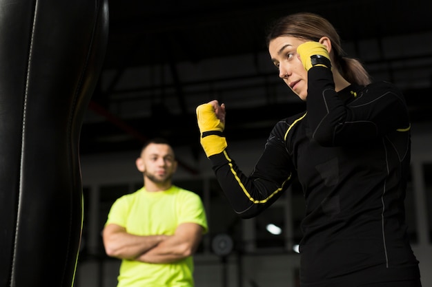 Seitenansicht des weiblichen Boxers übend mit dem defocused Traineraufpassen