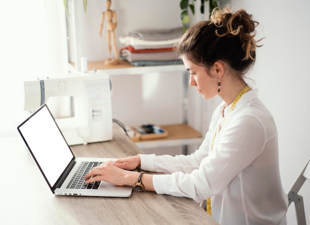 Kostenloses Foto seitenansicht des weiblichen schneiders unter verwendung des laptops