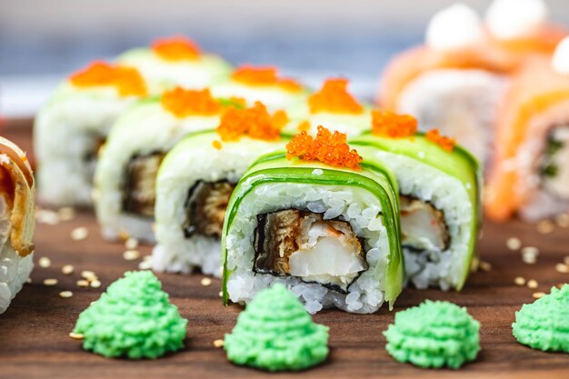 Seitenansicht Drachenrolle mit Gurken gebratenem Fisch Tobiko Kaviar Sesam und Wasabi auf einem Brett