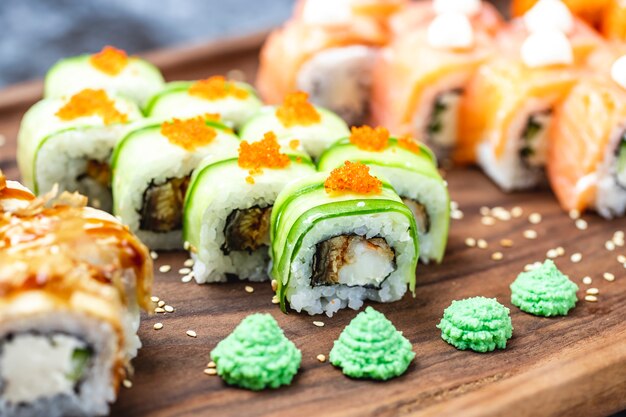 Seitenansicht Drachenrolle mit Gurken gebratenem Fisch Tobiko Kaviar Sesam und Wasabi auf einem Brett