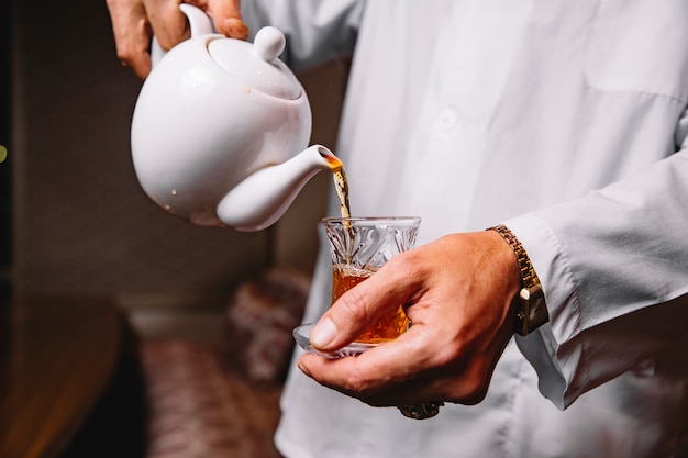 Seitenansicht ein Mann gießt Tee in ein Glas Armudu auf seine Hände