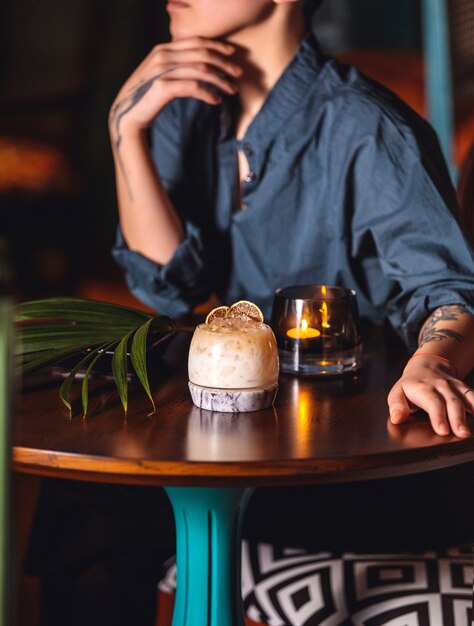 Seitenansicht eine Frau sitzt an einem Tisch mit einem Cocktail und einer brennenden Kerze