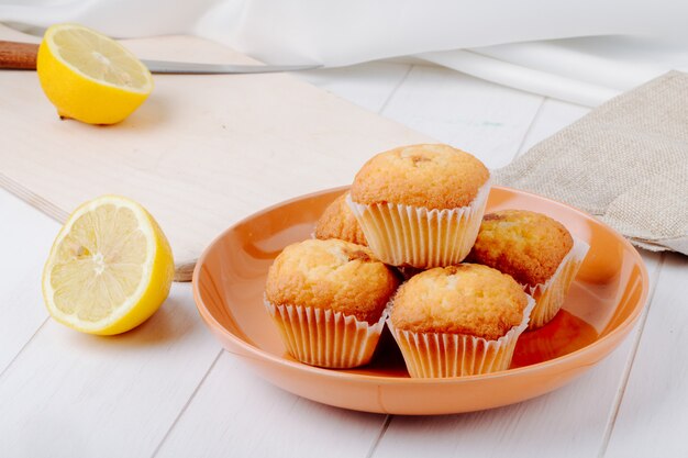 Seitenansicht eine halbe Zitrone auf einem Brett mit Cupcakes auf einem Teller