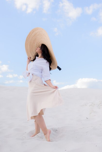Seitenansicht einer attraktiven Brünette mit großem Hut steht auf dem Sand