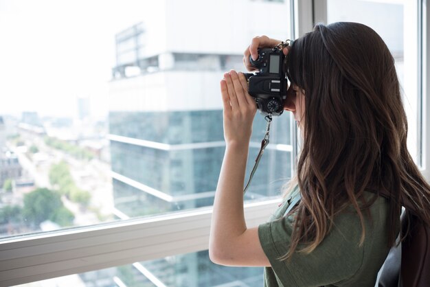 Seitenansicht einer Frau, die Fotos vom Fenster in der DSLR-Kamera macht