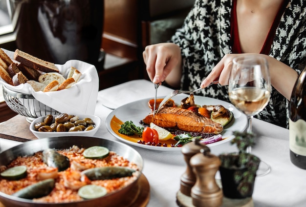 Seitenansicht einer Frau, die gebackenen Lachs mit Gemüse am Tisch isst