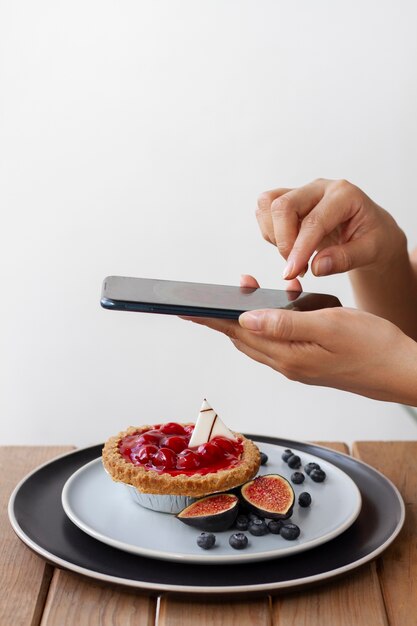 Seitenansicht einer Frau, die Obsttorte mit Smartphone fotografiert